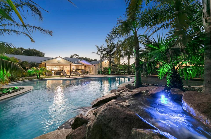 A kidney-shaped pool lit up at night. An social outdoor area is in the background.