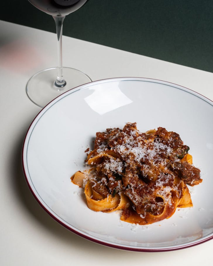 A bowl of pasta next to a glass of red wine on a crisp white tablecloth