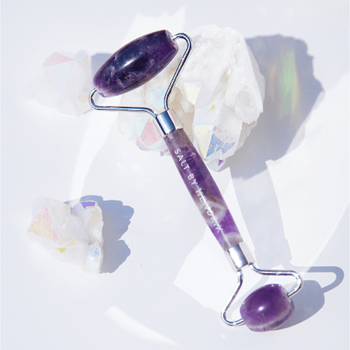 A purple amethyst face roller sitting on crystals