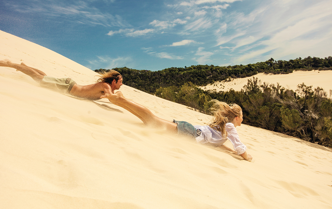 two people boarding down a sand dune