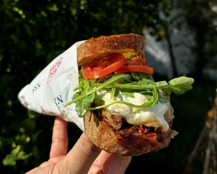 Someone holds a sandwich overflowing with fillings
