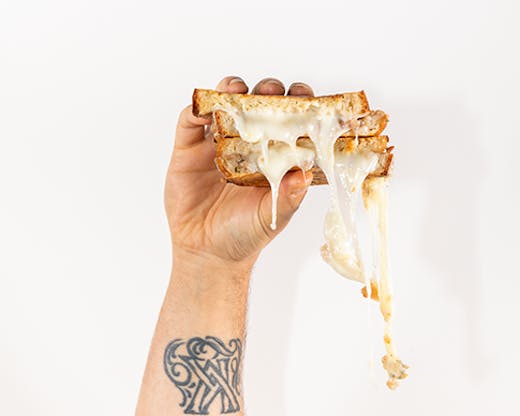 A cheese sandwich being held in one hand. The man's arm is covered in tattoos. 