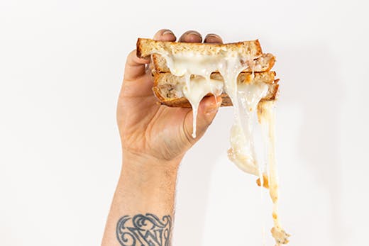 A cheese sandwich being held in one hand. The man's arm is covered in tattoos.