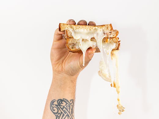 A cheese sandwich being held in one hand. The man's arm is covered in tattoos. 