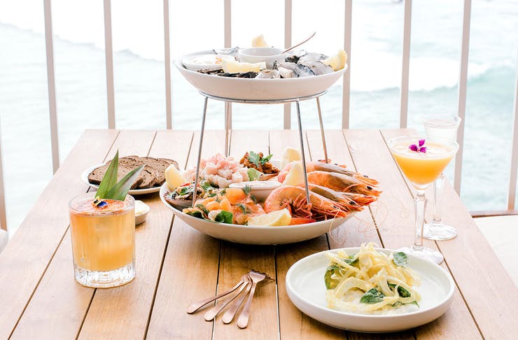 A tiered seafood platter on a table, overlooking the beach at Burleigh Heads.