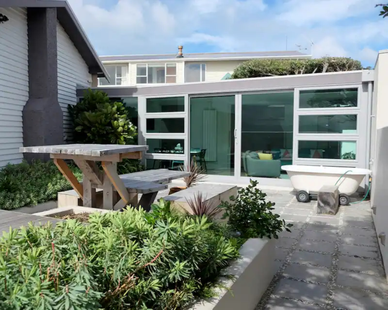 A view of the sunny outdoor area at the Seaside Haven featuring a picnic table and outdoor bath, and is one of the best airbnbs in Wellington.