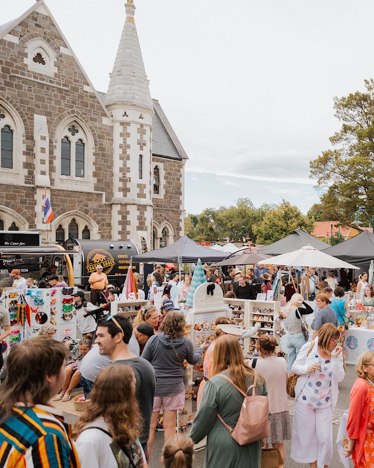 People wander Market Square beneath Gothic revival buildings, enjoying The Seekers MÄkete on a sunny day.
