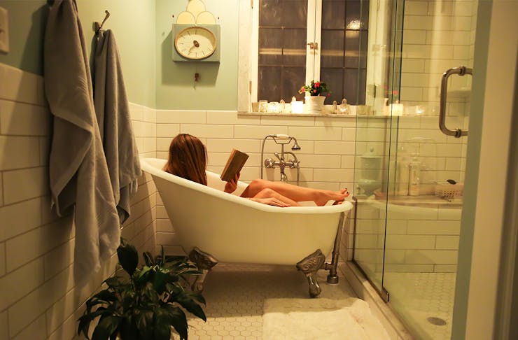 Woman in a bathtub in a homely bathroom, reading a book