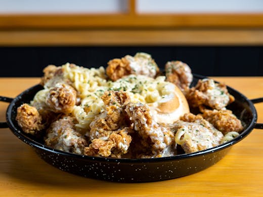 a tin bowl filled with fried chicken and pasta in a bread bowl