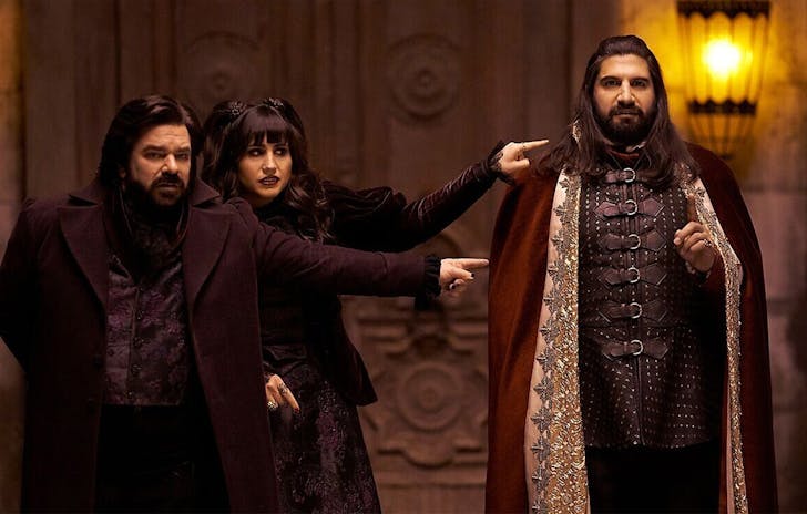 Three main characters from What we do in the shadows stand in an old parlour wearing capes and other old accoutrements.