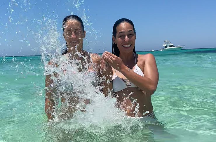 Two women standing in the ocean laughing with one splashing the water.