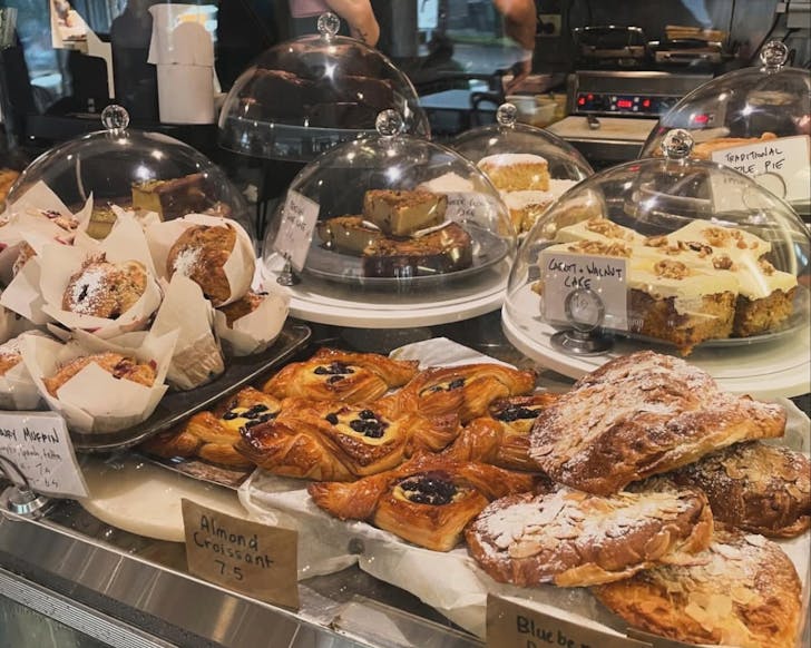A close up image of rows of freshly baked sweets in small display cases in front of a cafe counter.