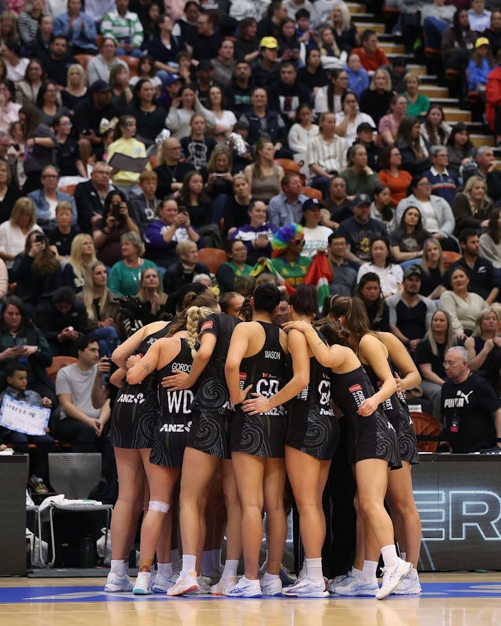 The Silver Ferns crowd in for a circle huddle in front of a grand stand audience indoors.