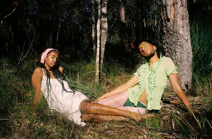 Two people wearing linen clothing and sitting in the grass, while basking in the sunlight.