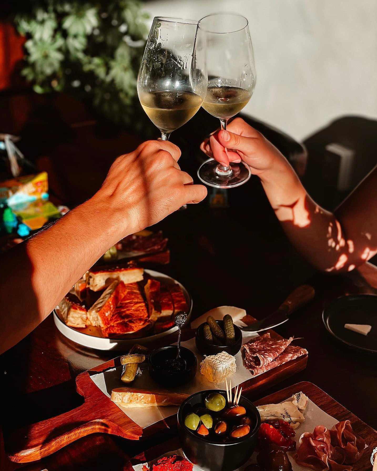 two glasses of white wine clinking over platters of antipasti treats at Six Ounces