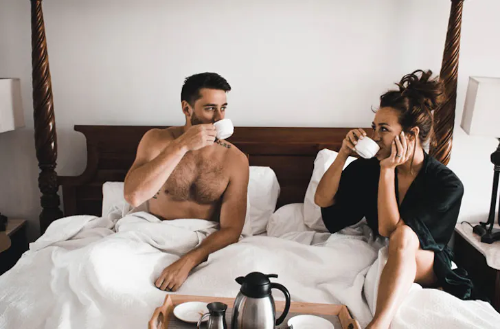 A couple sip tea in bed. 