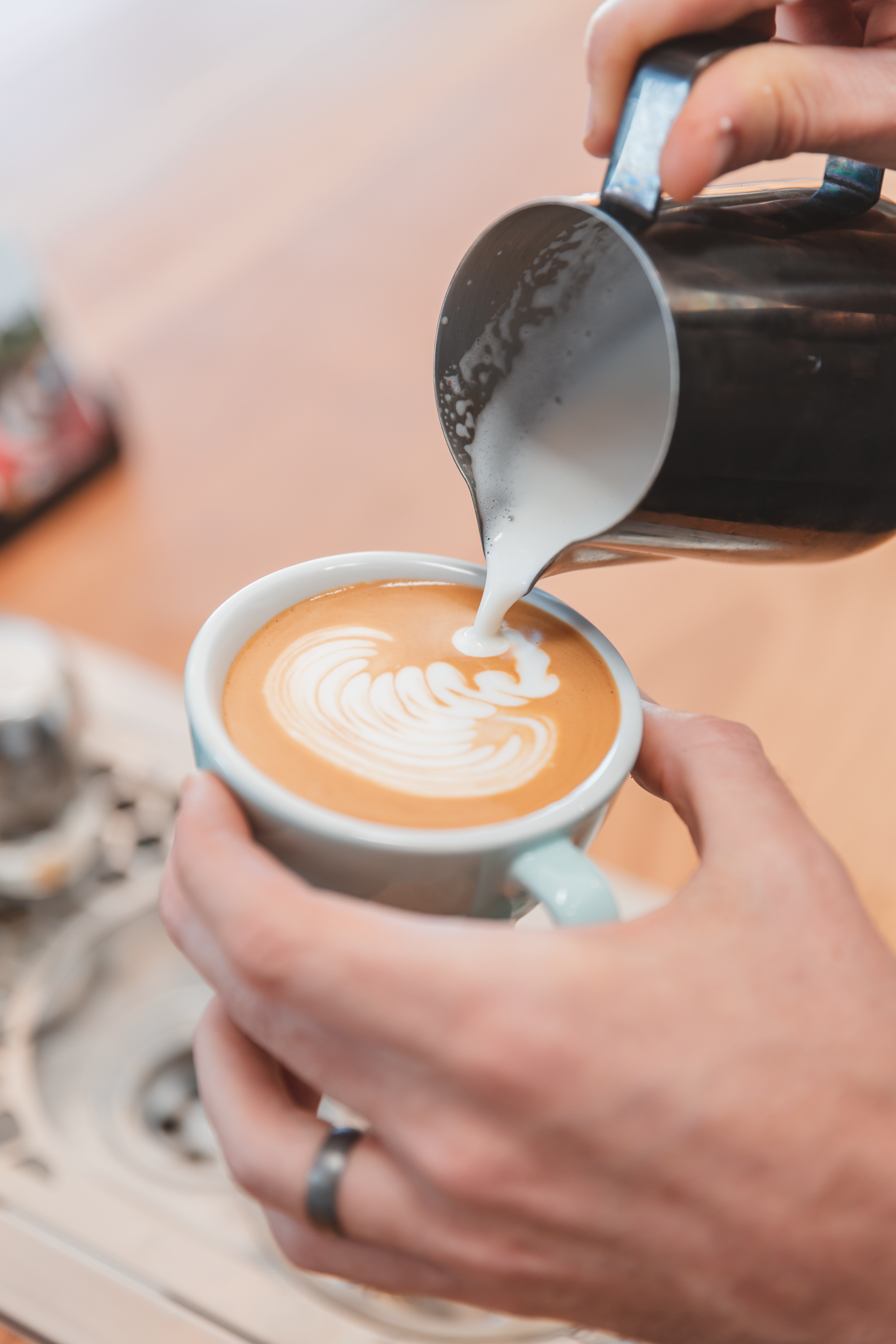 A hand holding a coffee cup and pouring milk into an artsy shape in the crema.