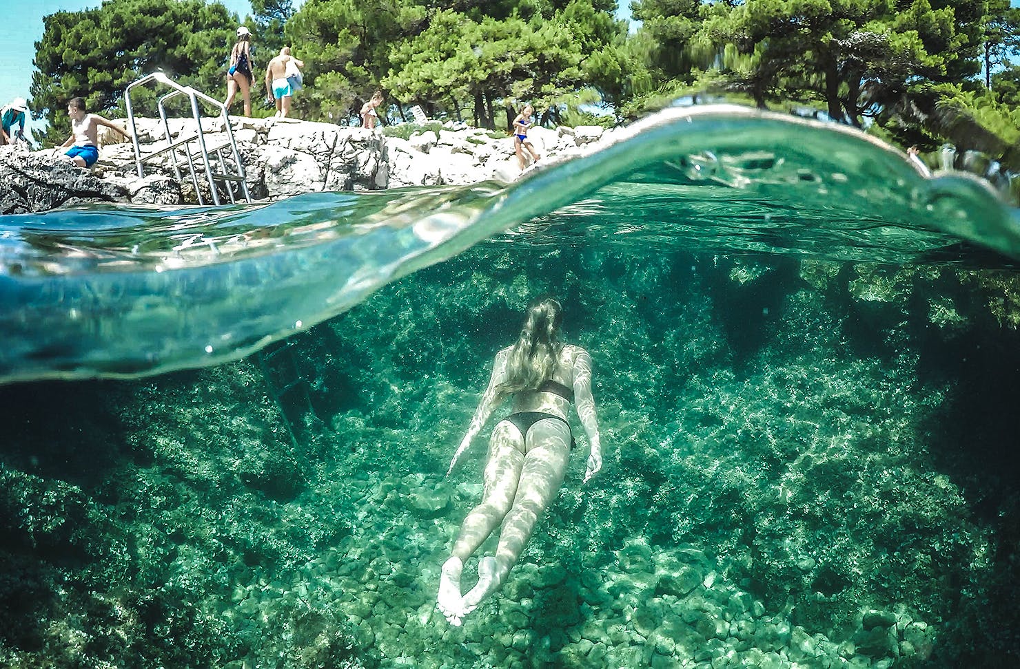 A woman swims through green water to the land above.