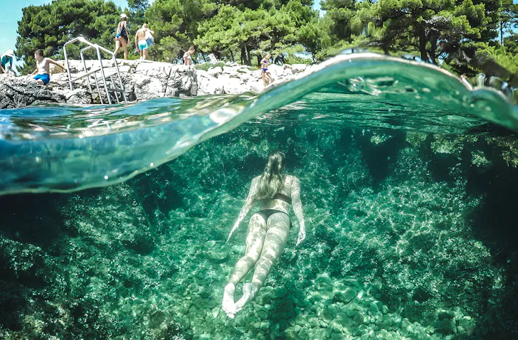 A woman swims through green water to the land above.
