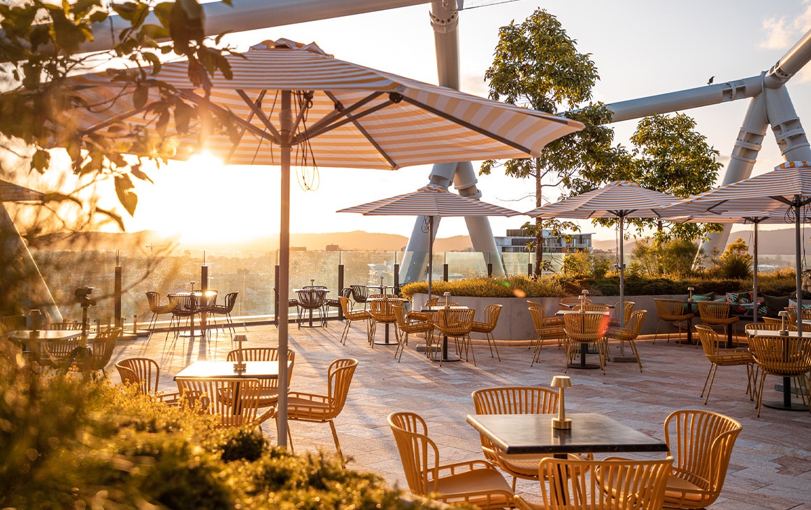 a rooftop space filled with yellow chairs, tables and striped umbrellas