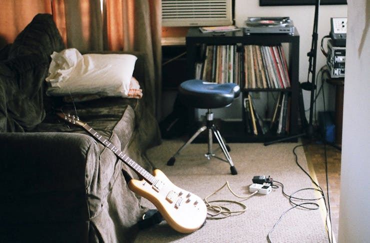 A cosy living room, with an electric guitar leaning against a couch and a shelf filled with old records. 