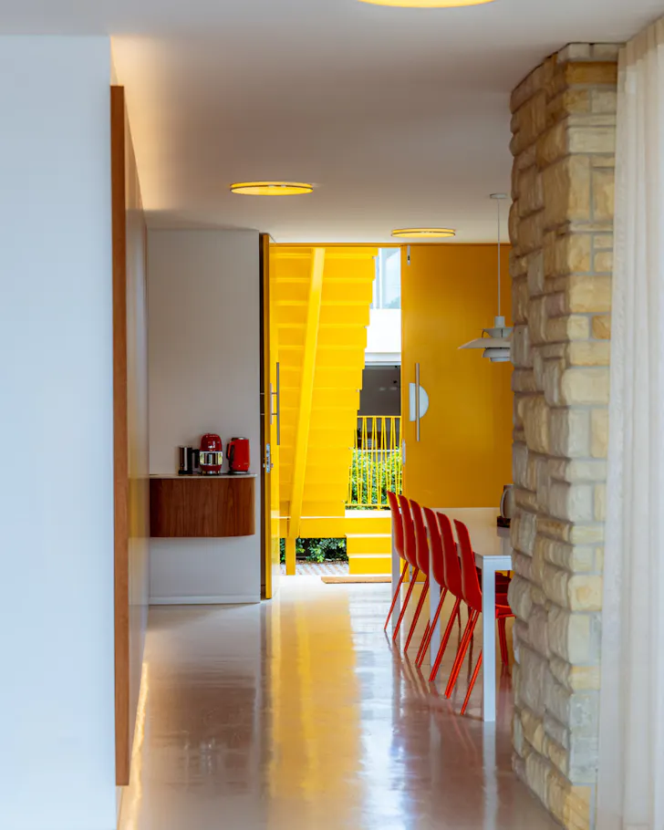 Modern mid-century interior with sandstone walls, red dining chairs and a striking yellow staircase.