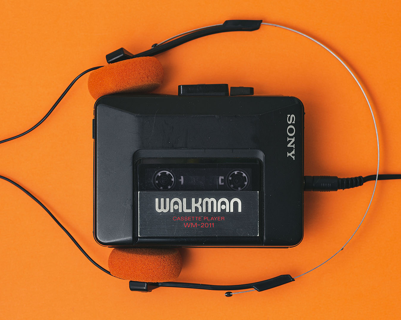 Old school cassette player with black and orange headphones on a bright orange background.
