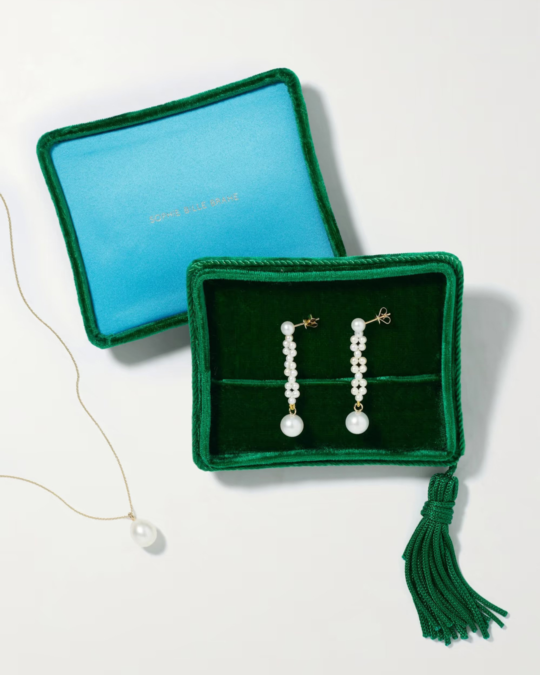 A green and blue velvet jewellery box with pearl earrings and a necklace.