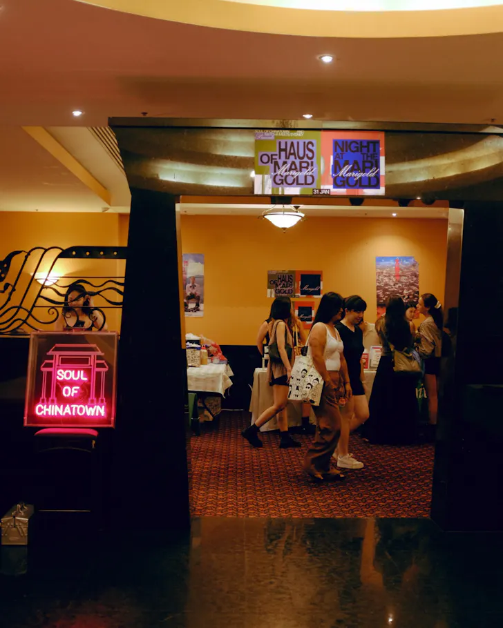 Visitors browse stalls inside a Soul of Chinatown community event, marked by a glowing neon sign at the entrance and showcasing local artists, makers and exhibitors.