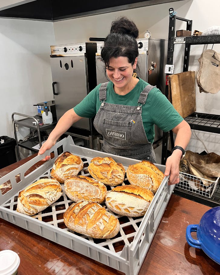 A woman lifts up a tray of freshly baked sourdough