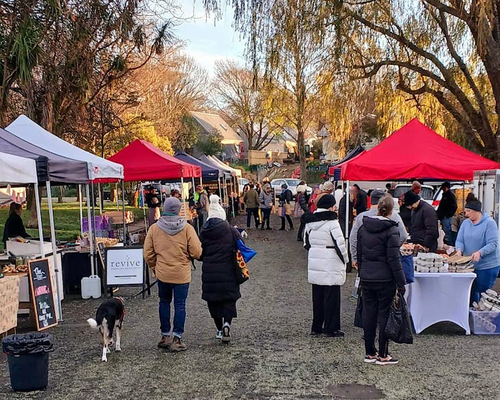 People, one couple walking their dog, stroll between South Christchurch Farmersâ Market stalls.