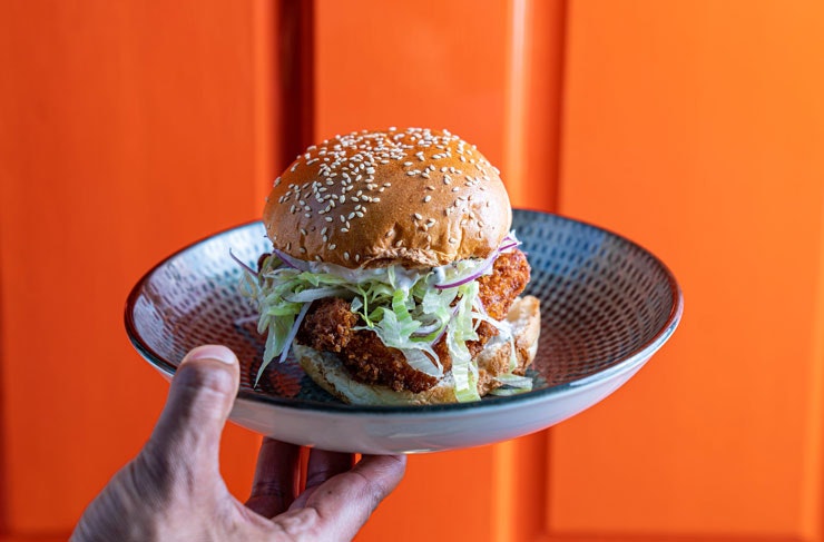 A fish burger on a plate with an orange background. 