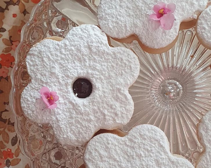 Three giant, flower-shaped, icing sugar-topped shrewburie cookies with jammy centres.