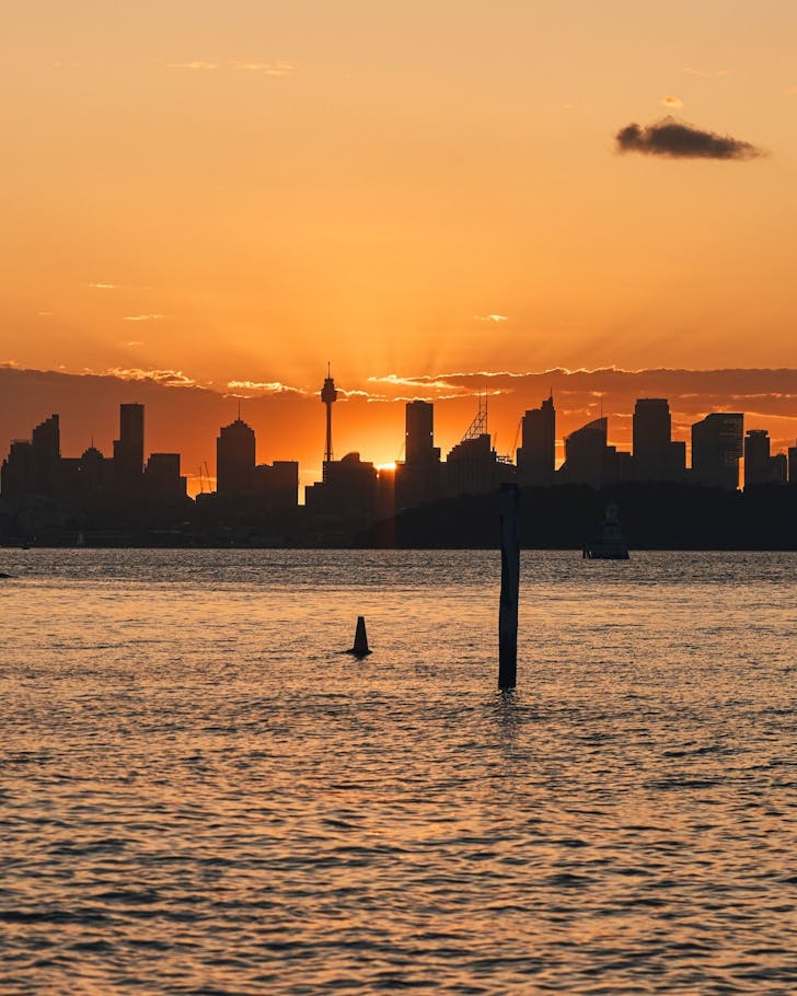 the sun setting behind the sydney cbd from camp cove