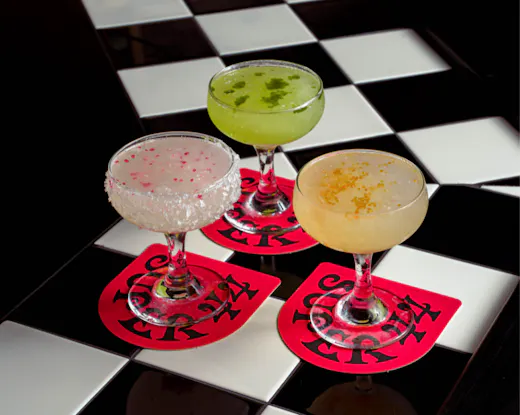 Three colourful margaritas from Super 44 served on a black-and-white tiled table, each showcasing vibrant fruit-forward garnishes.