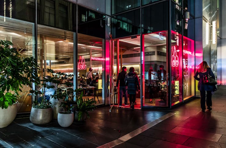 Iconic Melbourne restaurant Supernormal at night, it's neon lights reflecting in the rain on the street.