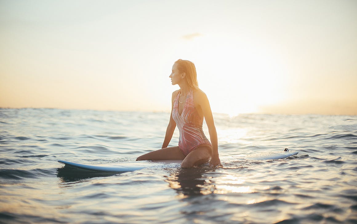 A girl sits on a surf board in the ocean waiting for the next wave.