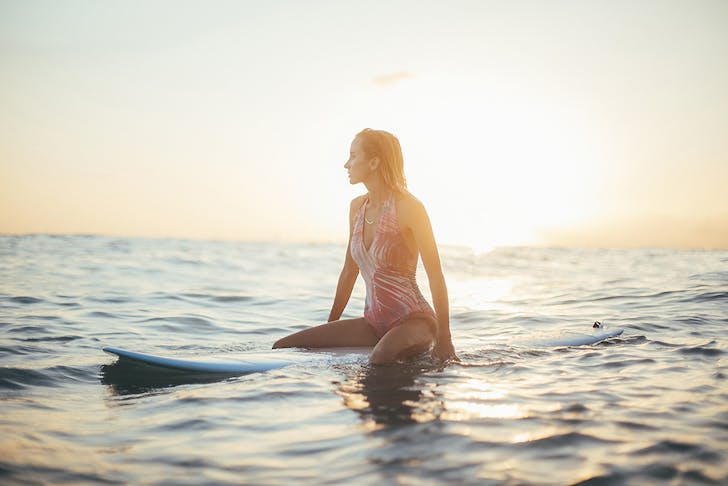 A girl sits on a surf board in the ocean waiting for the next wave.