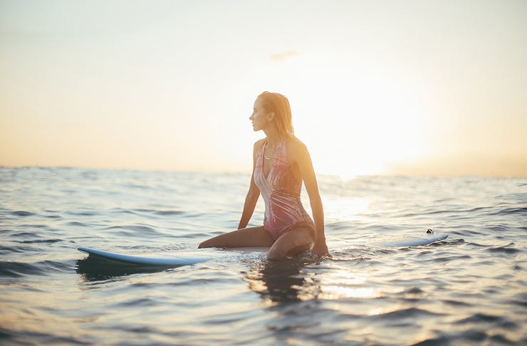 A girl sits on a surf board in the ocean waiting for the next wave.