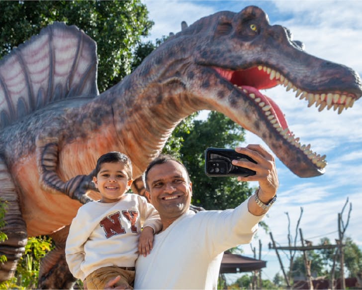Dad and son take a selfie in front of a large dinosaur statue at the Sydney Zoo.