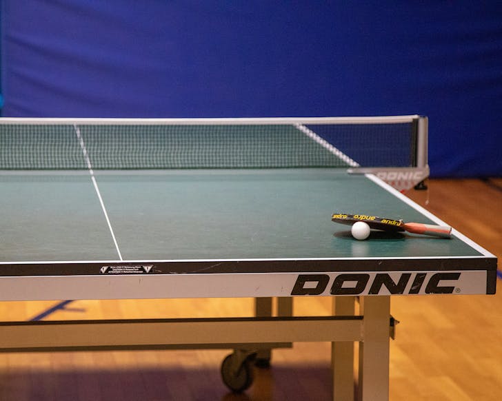 A single table tennis racket rests on top of the ping pong ball on the table.