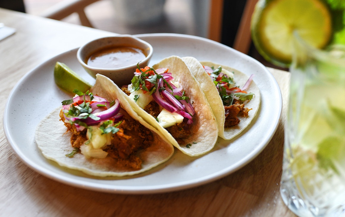 three tacos on a plate, a margarita in the foreground