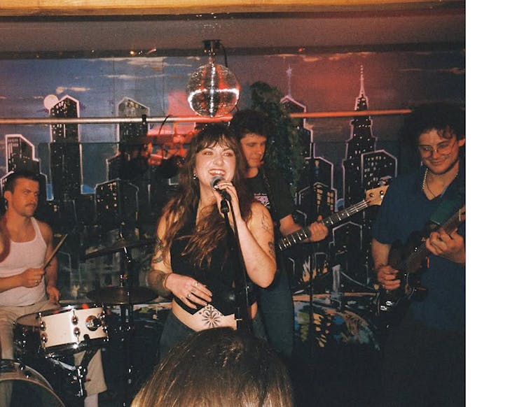 Tahini Bikini rock out on stage at a small indoor venue.
