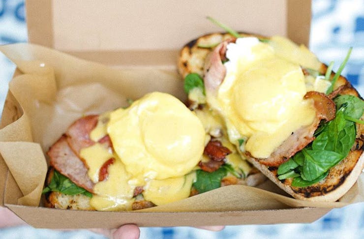 A takeaway box filled with eggs benedict on sourdough slices. 
