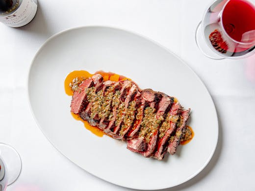 a sliced steak on a table with a glass of wine at tama brisbane