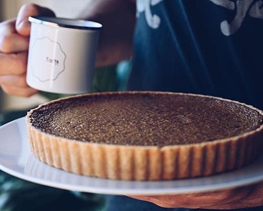 A tart on a plate next to a mug with a label that reads 