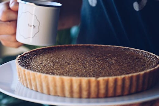 A tart on a plate next to a mug with a label that reads
