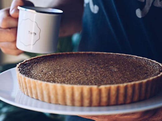 A tart on a plate next to a mug with a label that reads 