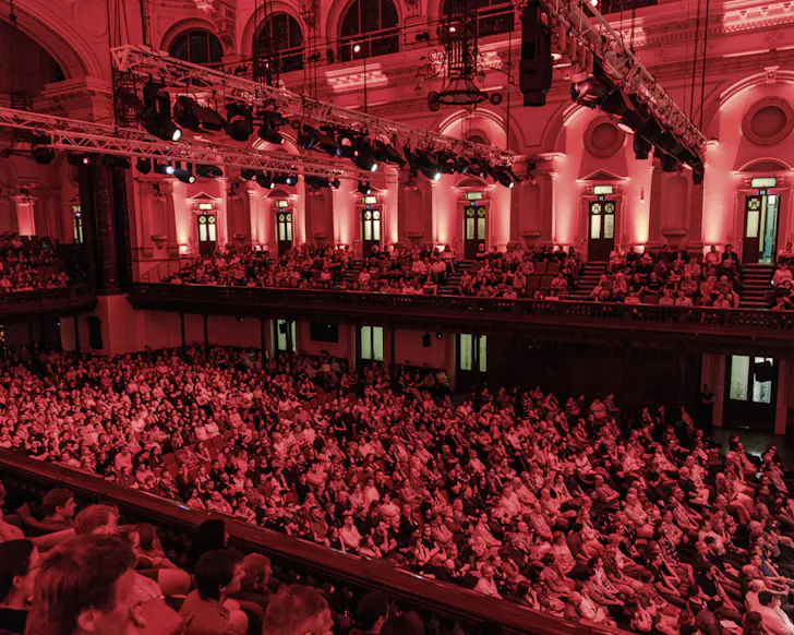 A packed audience fills the grand auditorium of Sydney Town Hall during the Festival of Dangerous Ideas, with the heritage interior illuminated in dramatic red lighting.