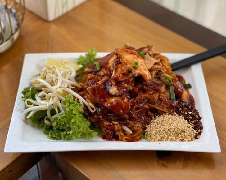 A saucy plate of chicken Pad Thai is accompanied by peanuts, chilli flakes, and crunchy beansprouts at Thai Box